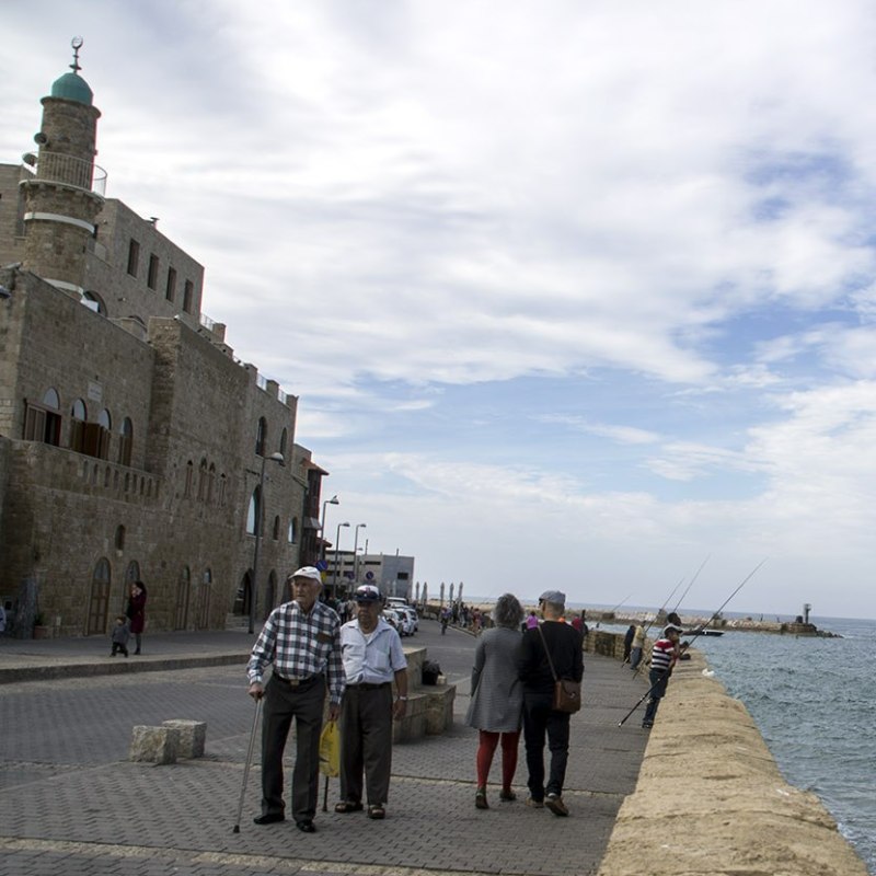 Jaffa tour: the seafront promenade of the ancient port People stroll along the Jaffa port promenade beside a stone mosque with a green-domed minaret, while anglers fish from the sea wall.