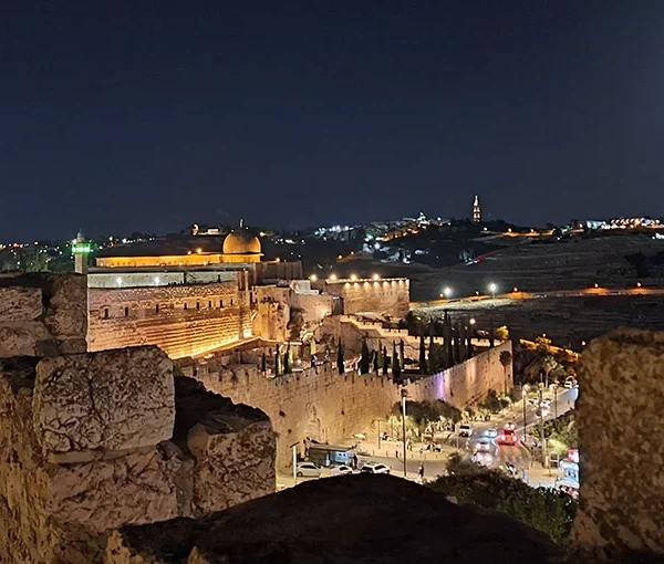Jerusalem's Old City walls at night, with the Dome of the Rock lit up and a full moon