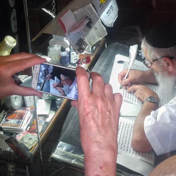 A traveler photographs a Torah scribe writing a scroll with a quill